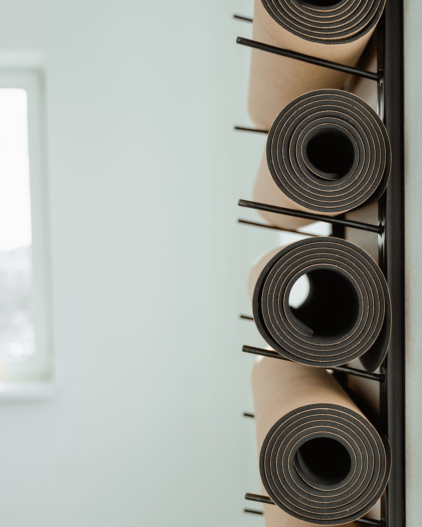 Rolled exercise mats stacked on a rack in a bright, empty studio.